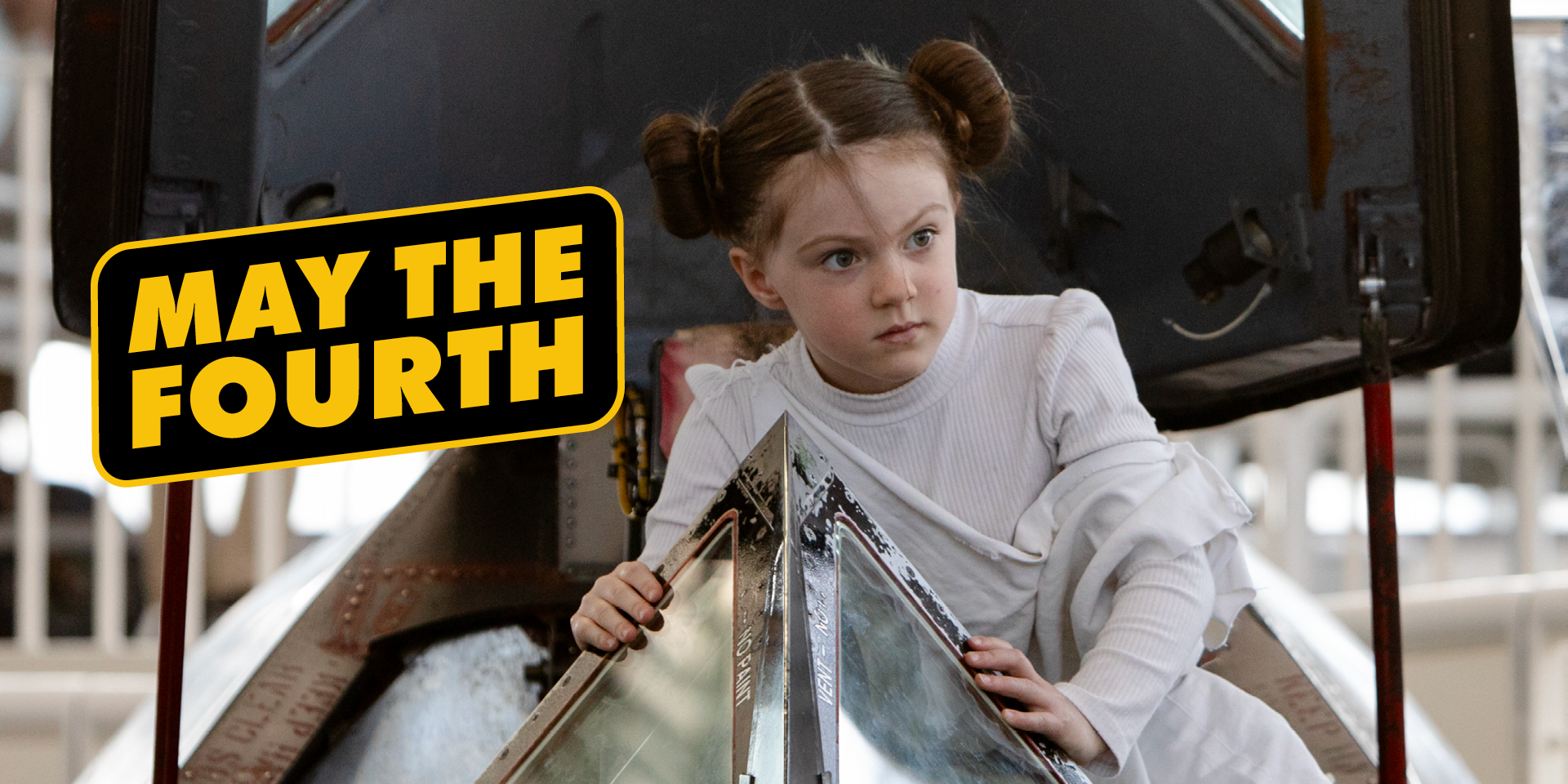 Little girl dressed as Princess Leia from Star Wars climbing into an SR-71 cockpit at The Museum of Flight. May the Fourth in Star Wars inspired yellow font on black background